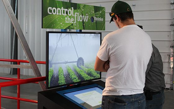 Man in front of a large display watching a movie about watering farmland.